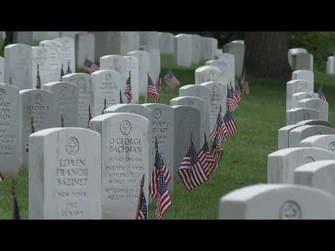 Military members place flags at headstones along Arlington National Cemetery